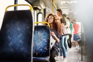 Young pretty woman is sitting on a bus seat and looking through the window while holding her bag on her lap.